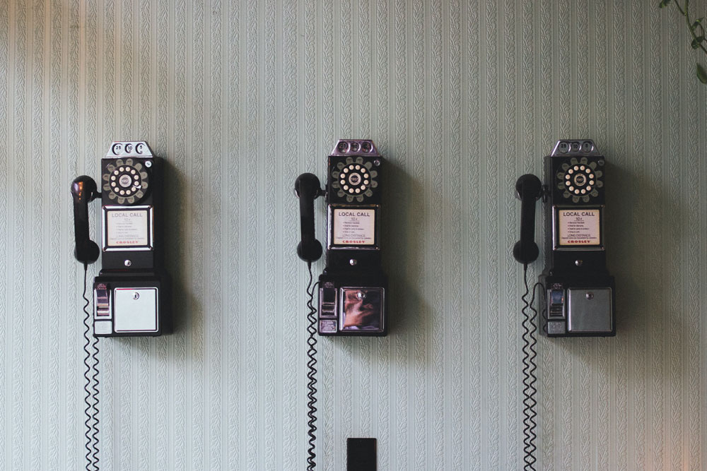 Three old telephones on the wall with striped wallpaper