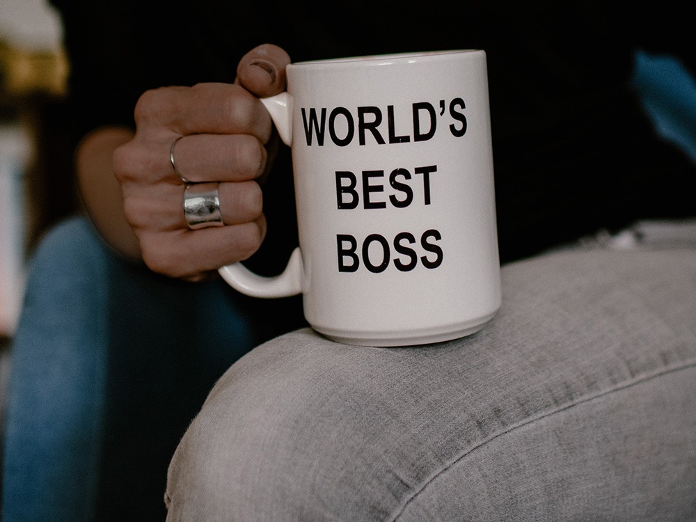 A hand holds a white mug, which reads "World's Best Boss"
