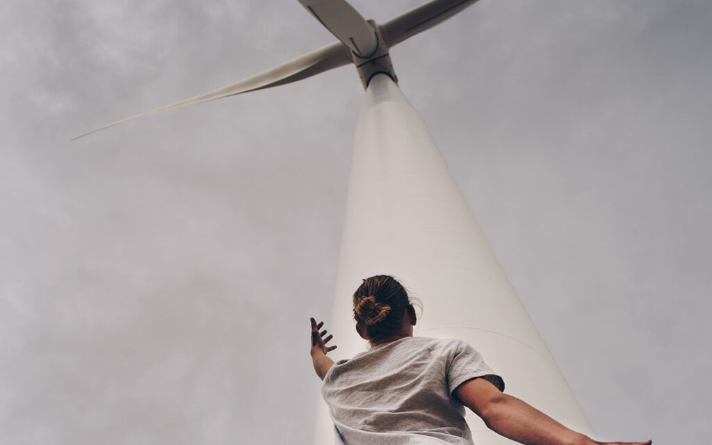 Woman looking up at a wind turbine, she is holding her hands up, motioning towards the turbine.