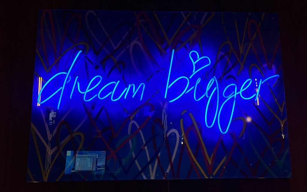 Blue neon sign that reads, "Dream Bigger"