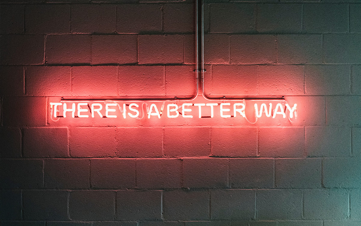 pink neon sign that reads "There is a better way" mounted on a cinderblock wall
