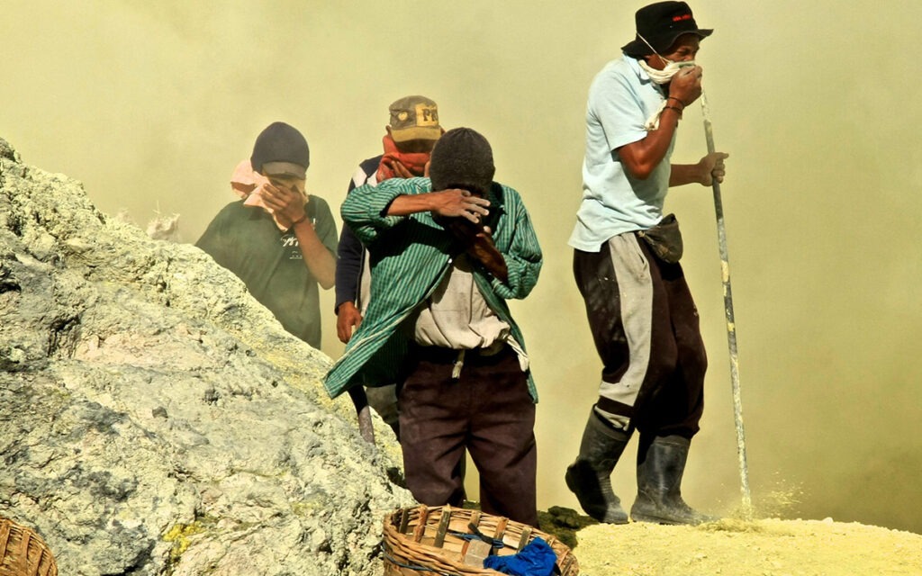 Mine workers in Indonesia wearing cloth masks and walking around in swirling dust.