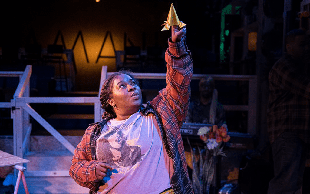 A performance photogrpah from ak payne’s play “Amani”, showing a Black girl holding up gold spaceship model