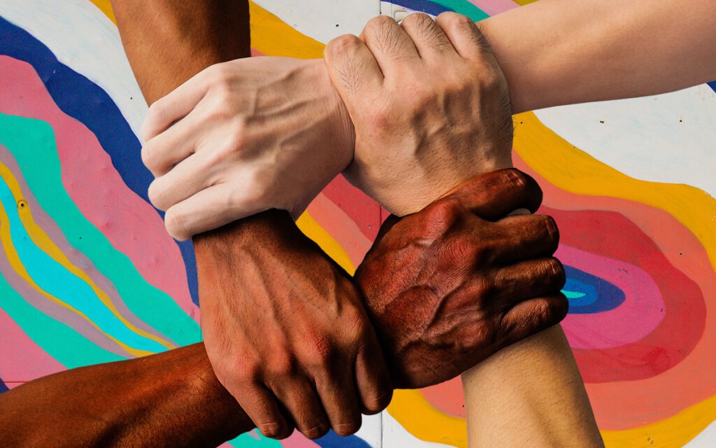 Four hands of different colors holding each others wrists, over a colorful backgorund.