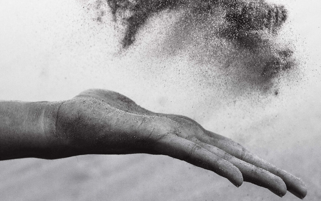 A black and white photo of a hand throwing sand into the air