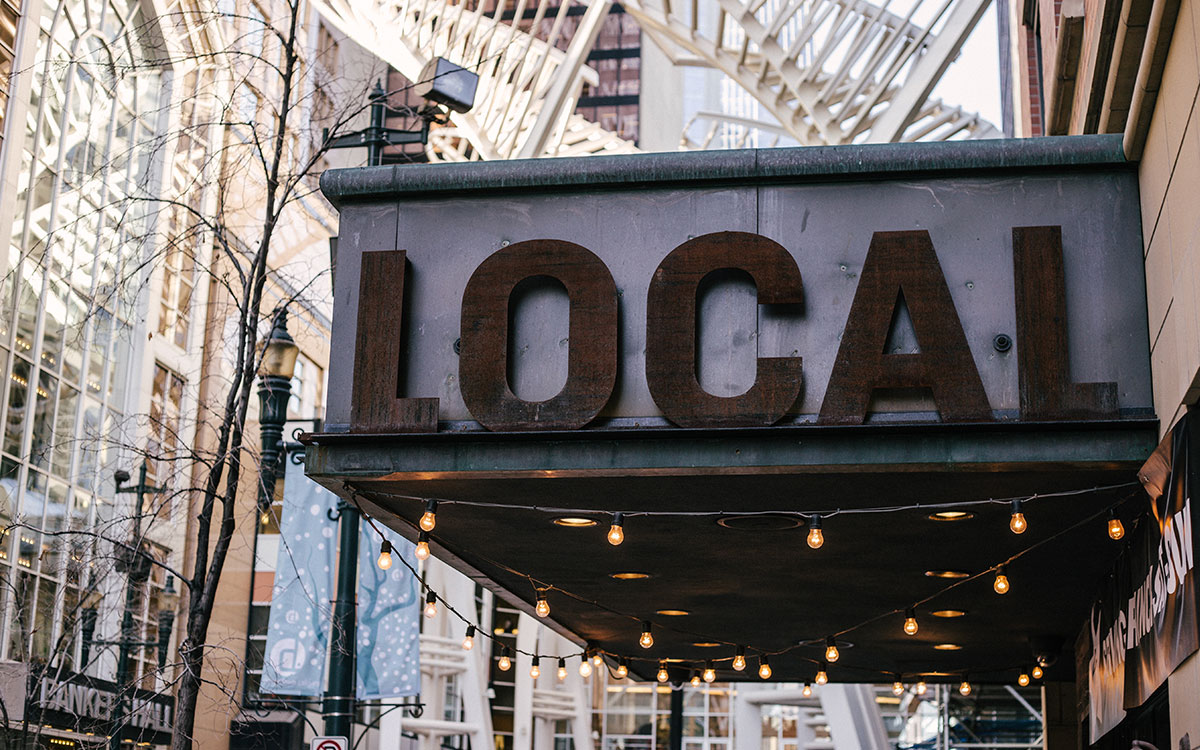 A business awning against a city backdrop, that reads "LOCAL" in wooden letters.