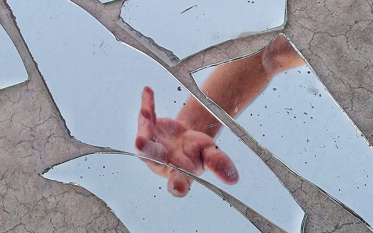 A hand reaching over shards of a broken mirror
