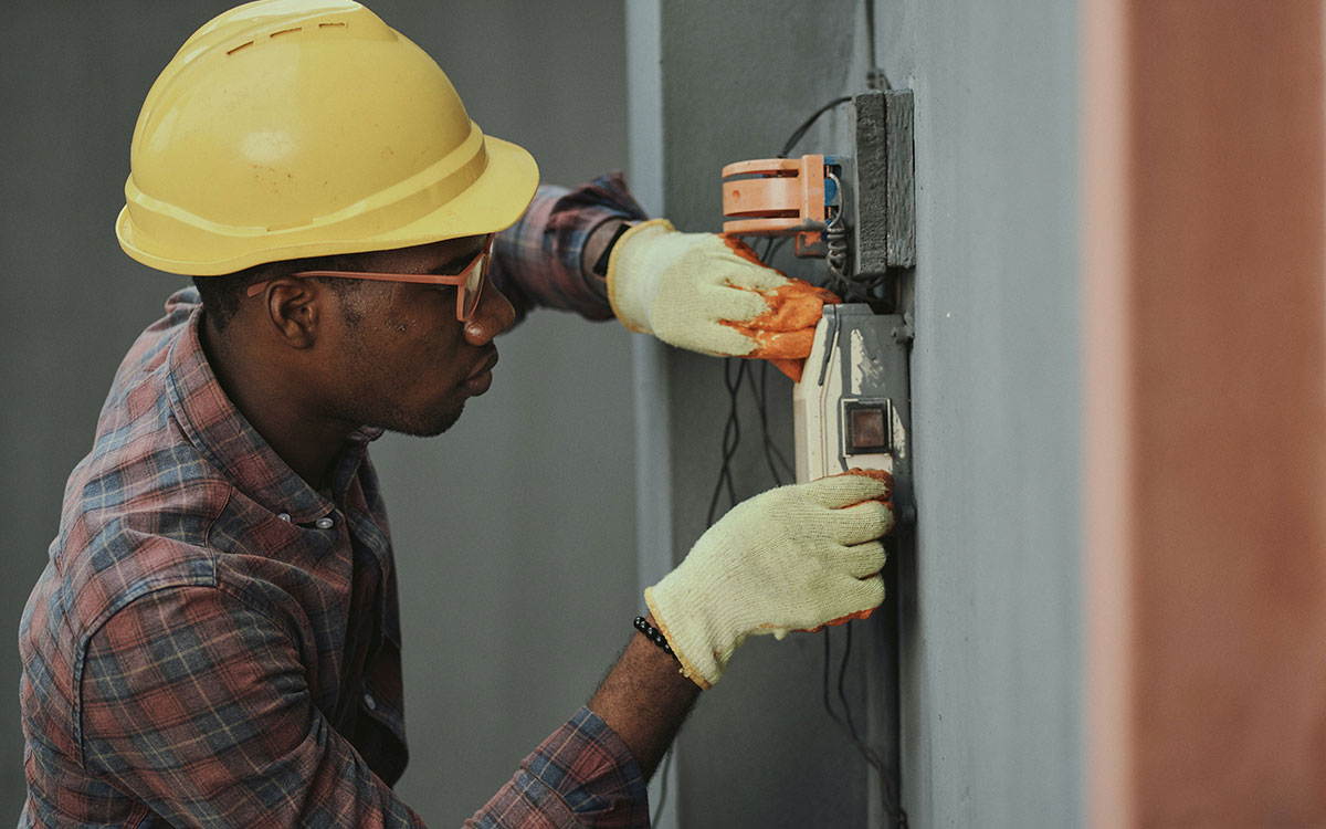 Black repair man with yellow hard hat working on an electrical outlet