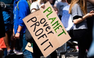 A person holding a cardboard sign that reads, “Planet Over Profit”