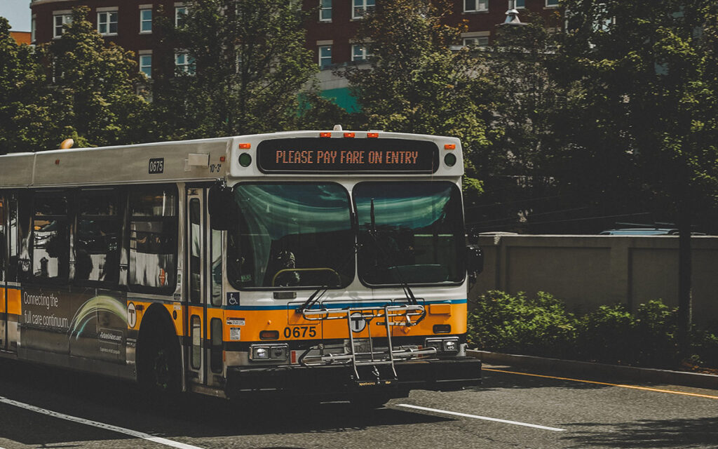 MBTA bus driving down the street. The words “Please pay fare on entry” are displayed in the marquee on the front of the bus.