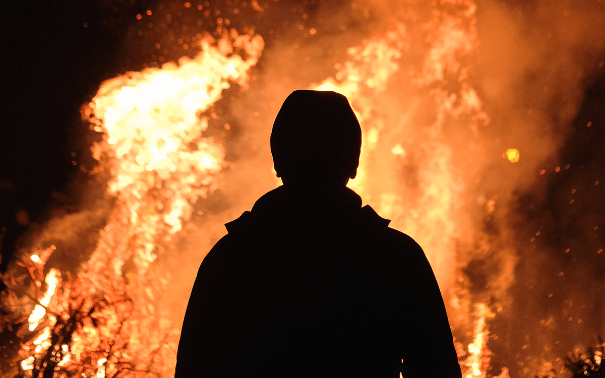 A silhouette of a man standing in front of a blazing forest fire.
