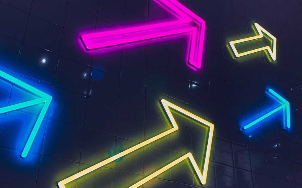 An arrangement of brightly colored neon-light arrows, pointing upwards.