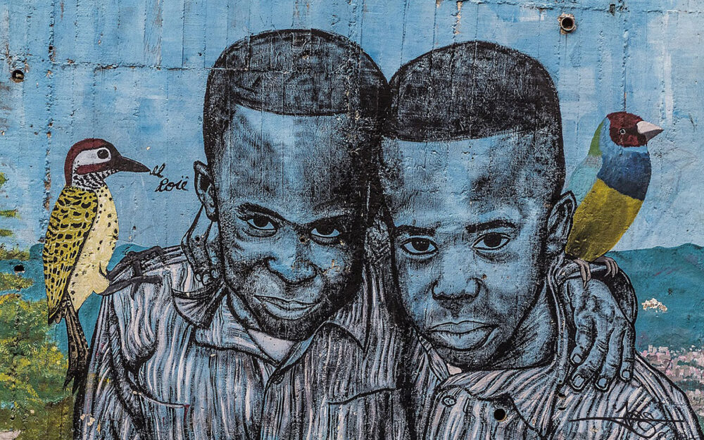 Mural of two young Black boys with colorful birds on their shoulders. They are smiling with their arms around each other.