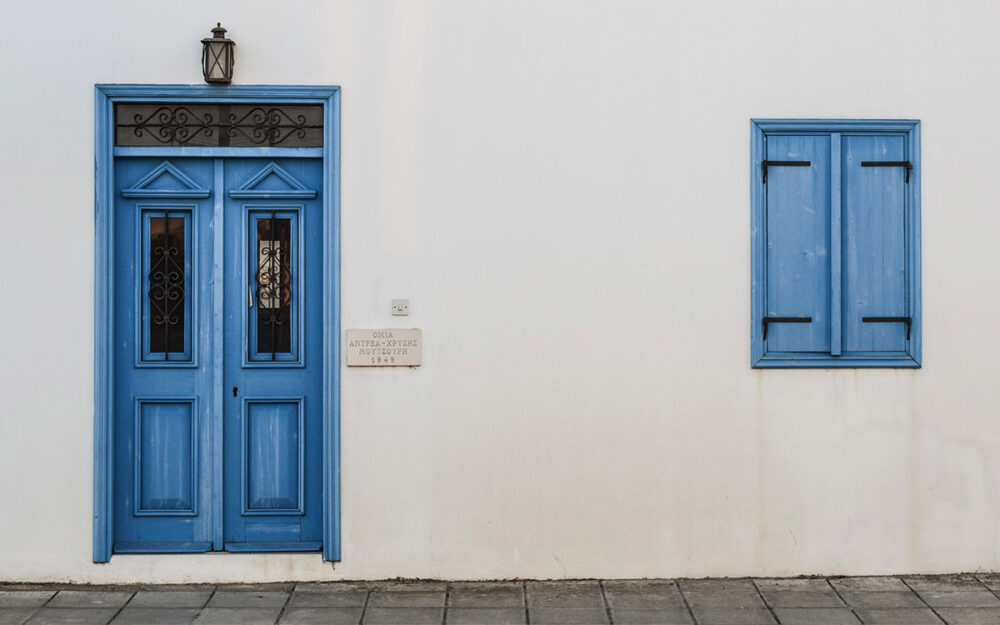 An ornate, blue wooden door and blue shuttered window set on a white wall.