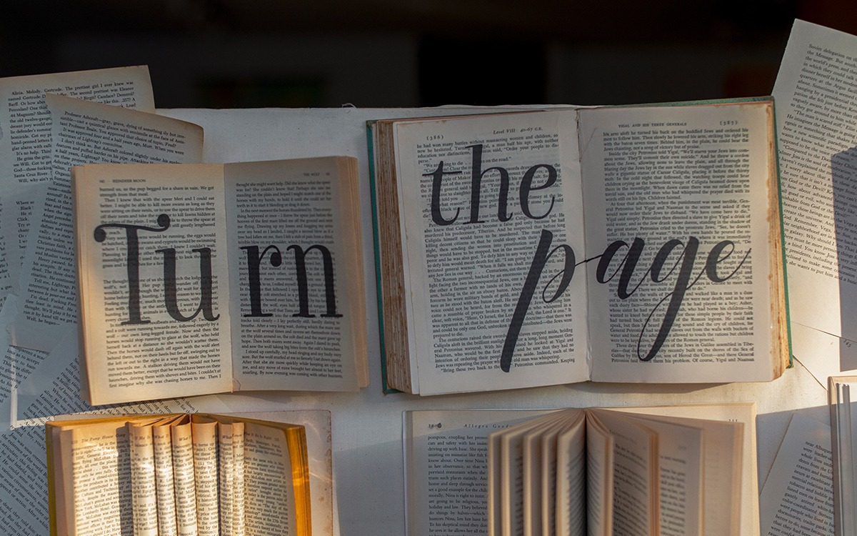 A pile of open books. The words, “Turn the Page” are written in large letters across the book pages.