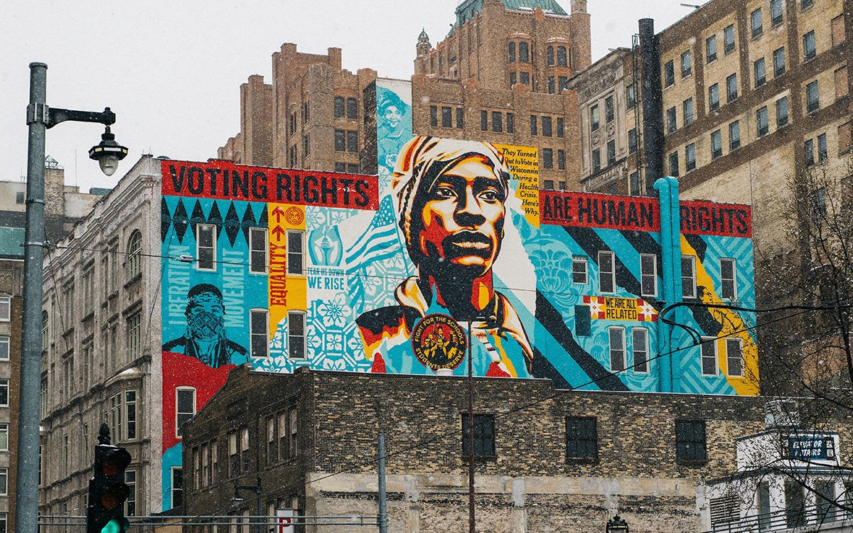 A painted mural on the side of a brick building that reads, “Voting rights are human rights”. The mural shows a determined-looking woman.