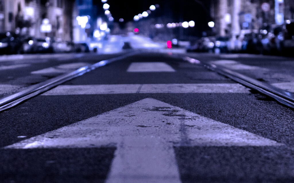 A painted white arrow, facing forward on a dimly-lit street at night