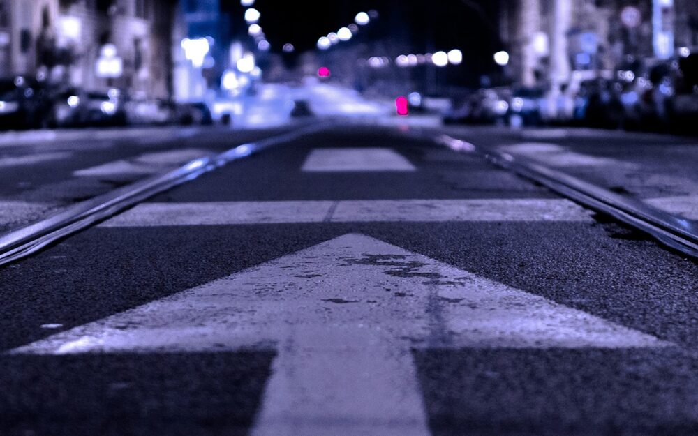A painted white arrow, facing forward on a dimly-lit street at night
