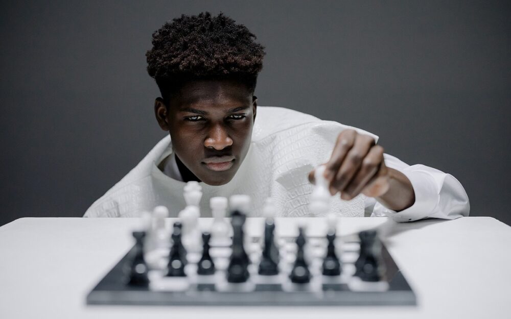 A black man with a high-tapered fade concentrating on a game of chess. He is putting his piece into play.