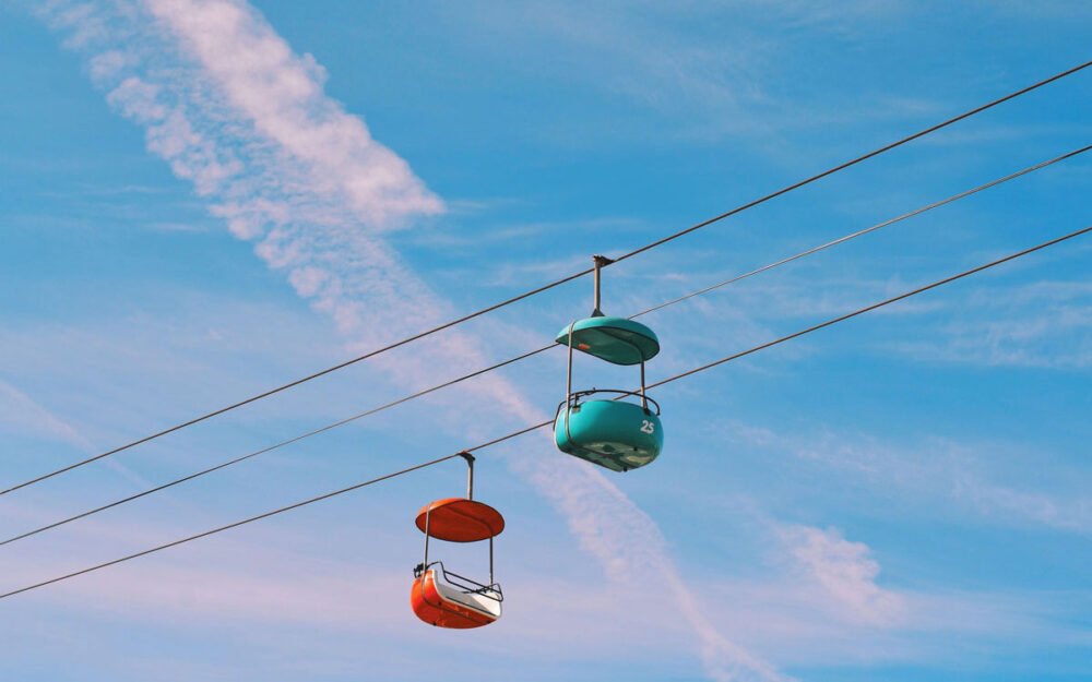 Two red and blue cable cars zipping past each other, against a blue sky.