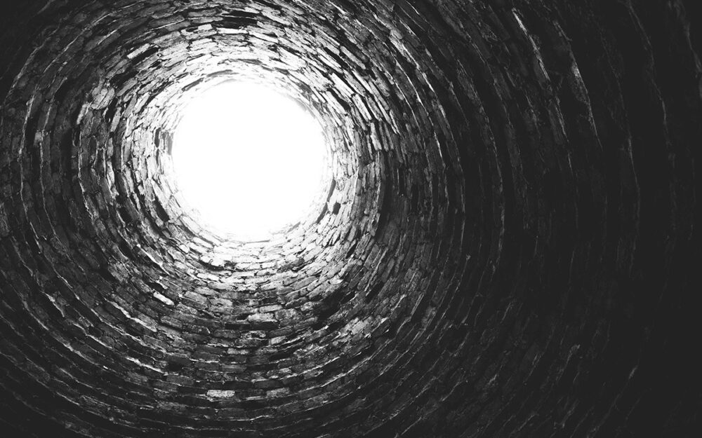 A Black in white photo of the opening of a well, looking up from inside of the well.