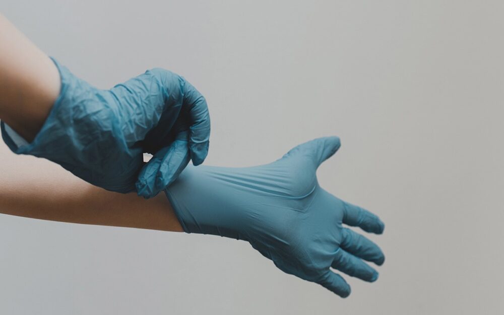 A person’s hands pulling on a pair of blue rubber gloves