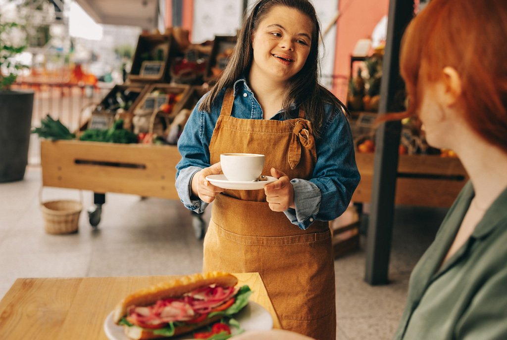 Smiling waitress with down syndrome serves a customer in a cafe.