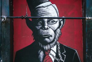 A mural of a black and white monkey wearing a fez, with a chain around his neck. The monkey is looking away with a sad look.