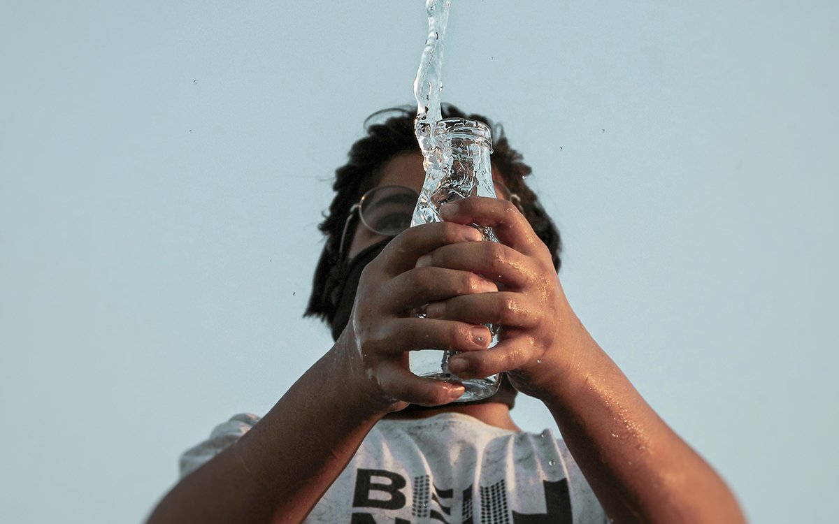 An Indian man tosses water up into the air, from a glass bottle.