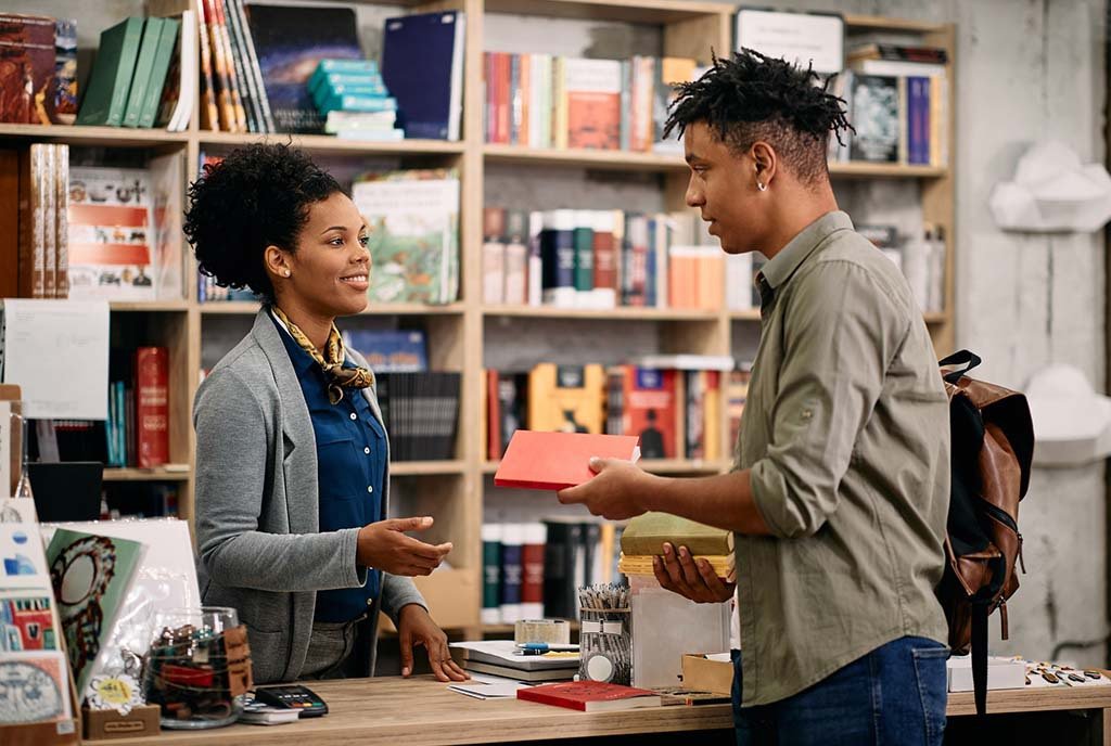 Young Black man returning book to a librarian at public library