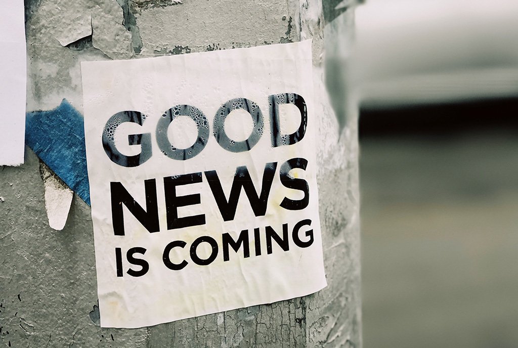 A laminated paper sign taped to a post. The sign reads, “Good News Is Coming”