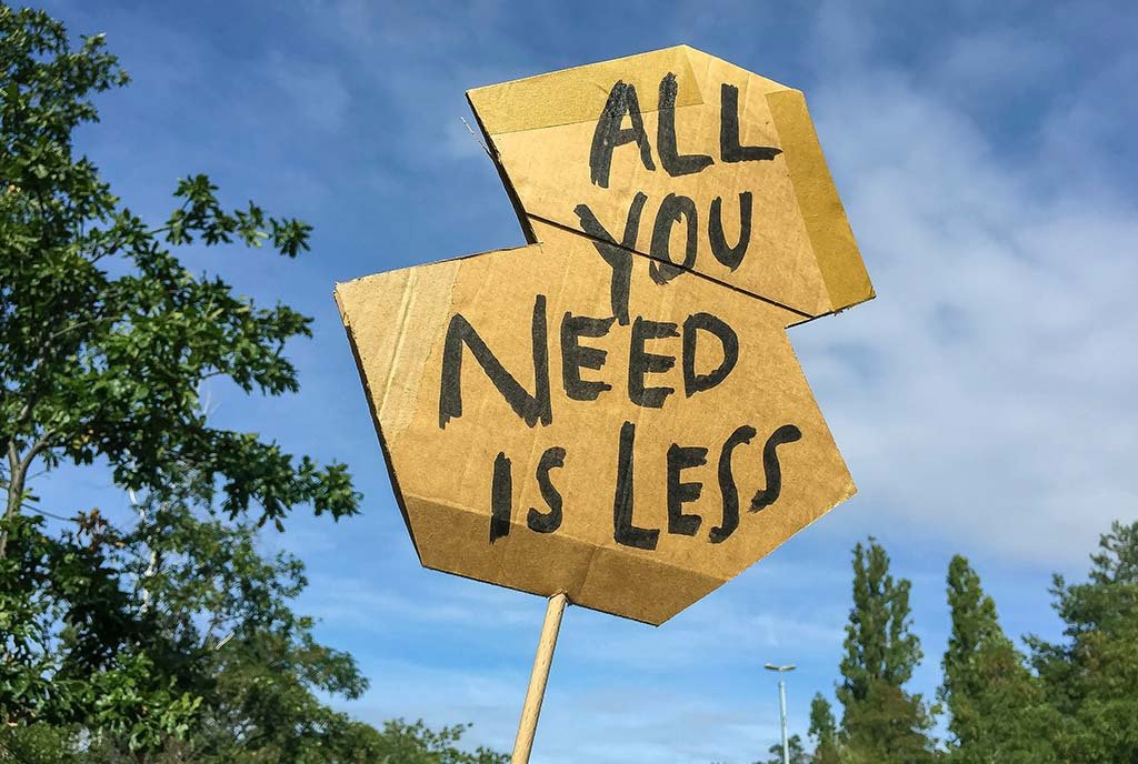 A cardboard sign in the air that reads, “All You Need is Less”