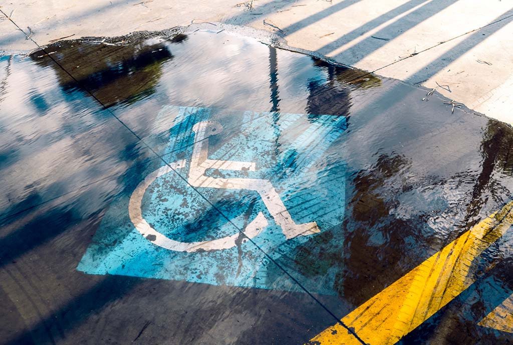 A blue handicapped sign painted on the flooded ground of an outdoor parking lot.