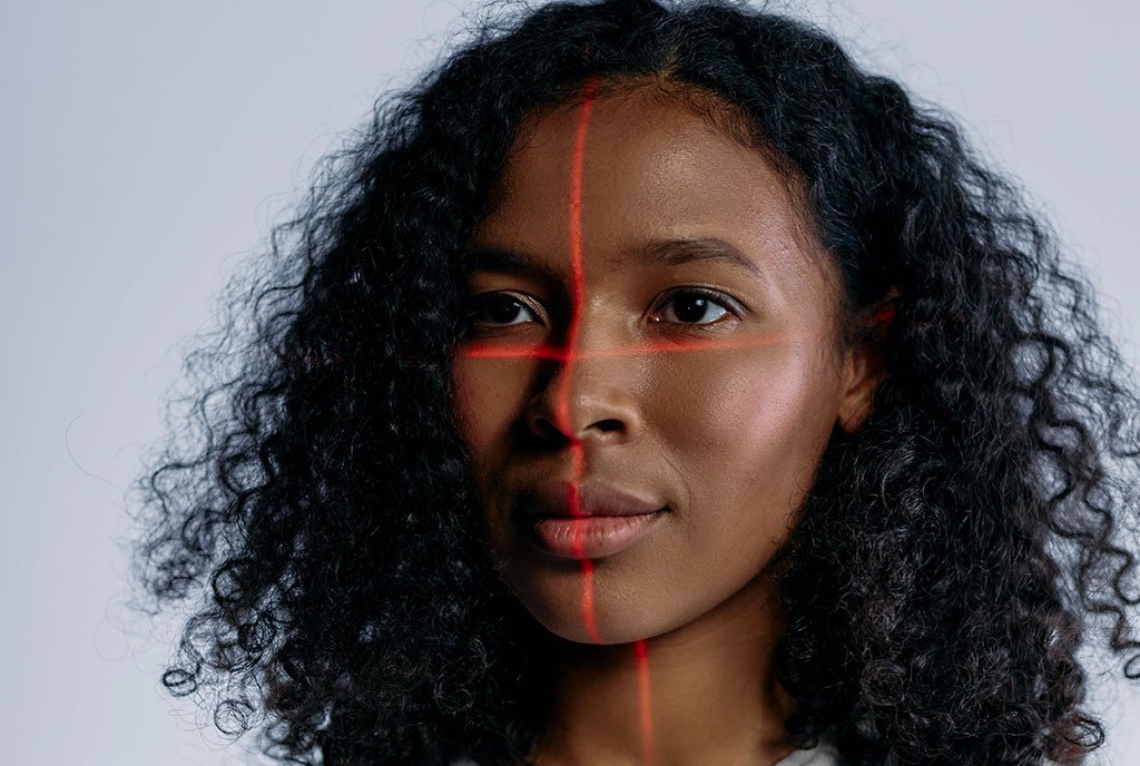 A Black woman with wavy hair who has a the projection of a red laser scanning her face.