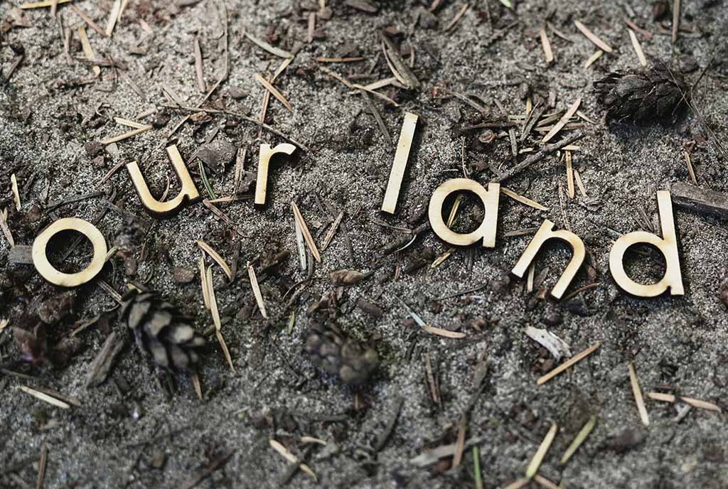 A section of dirt ground, with "Our Land" spelled in wooden laser cut letters