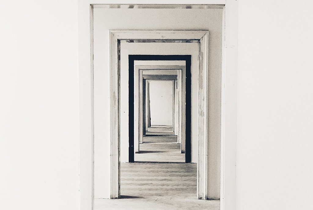 A photography looking down a hallway with multiple, aligned door frames. All door frames are white, except for one in the middle which is black.