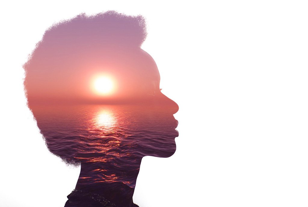 The sihoutte of a Black woman with an Afro is in profile, In the silhoutte, there is the warm image of a sun setting over the ocean.