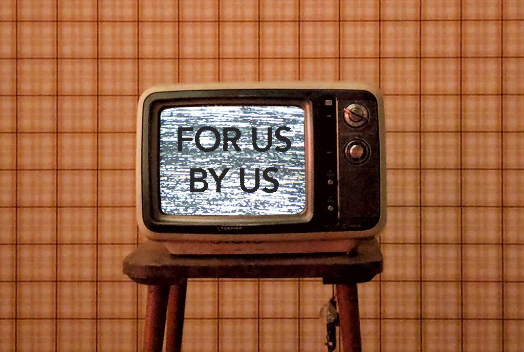 An antique television set in with grainy, static words on the screen reading, “For Us By Us”.