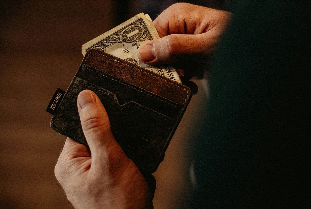 A hand reaching into a wallet and pulling out a single dollar bill.