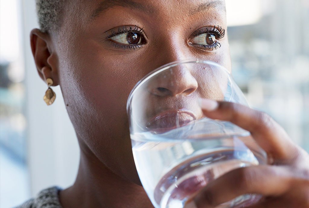A Black woman with cropped hair drinking a glass of water and looking off into the distance.