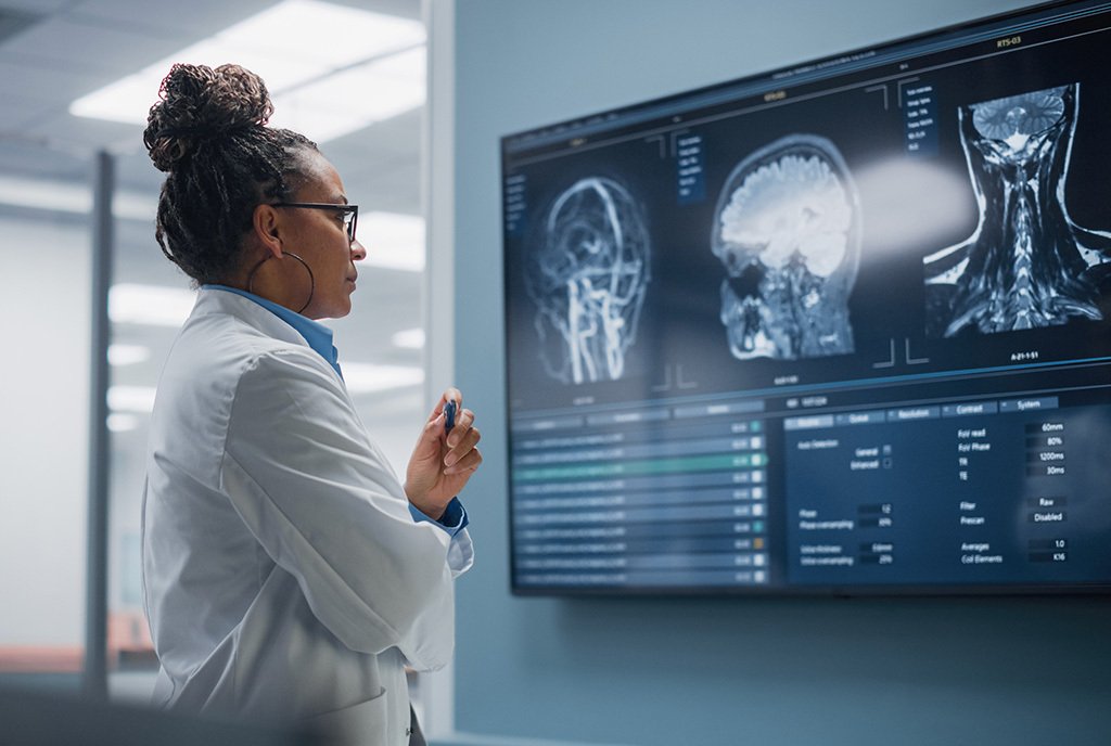 A confident Black female neurologist looking at a TV screen with MRI scans of brain images.