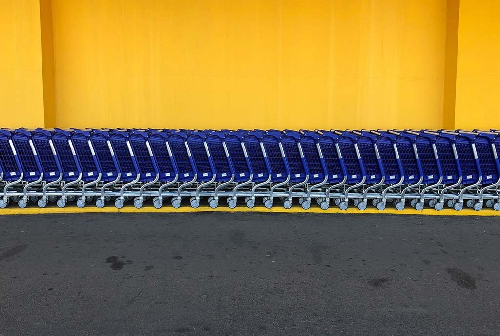 A neatly tucked line of blue Walmart shopping carts, against the yellow exterior wall of a Walmart.