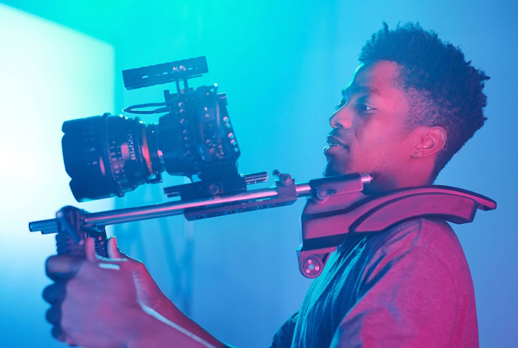 A Black man holding a video camera with a blue light in the background.