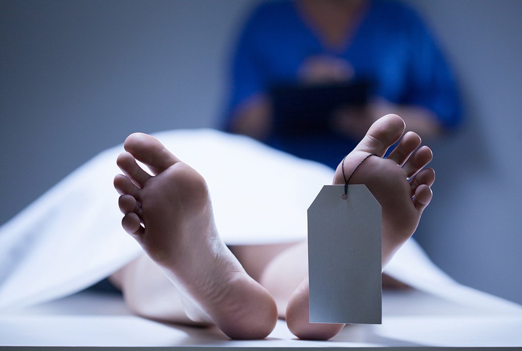 The exposed feet of a corpse lying on a coroner’s table, with a blank identification tag around the big toe.