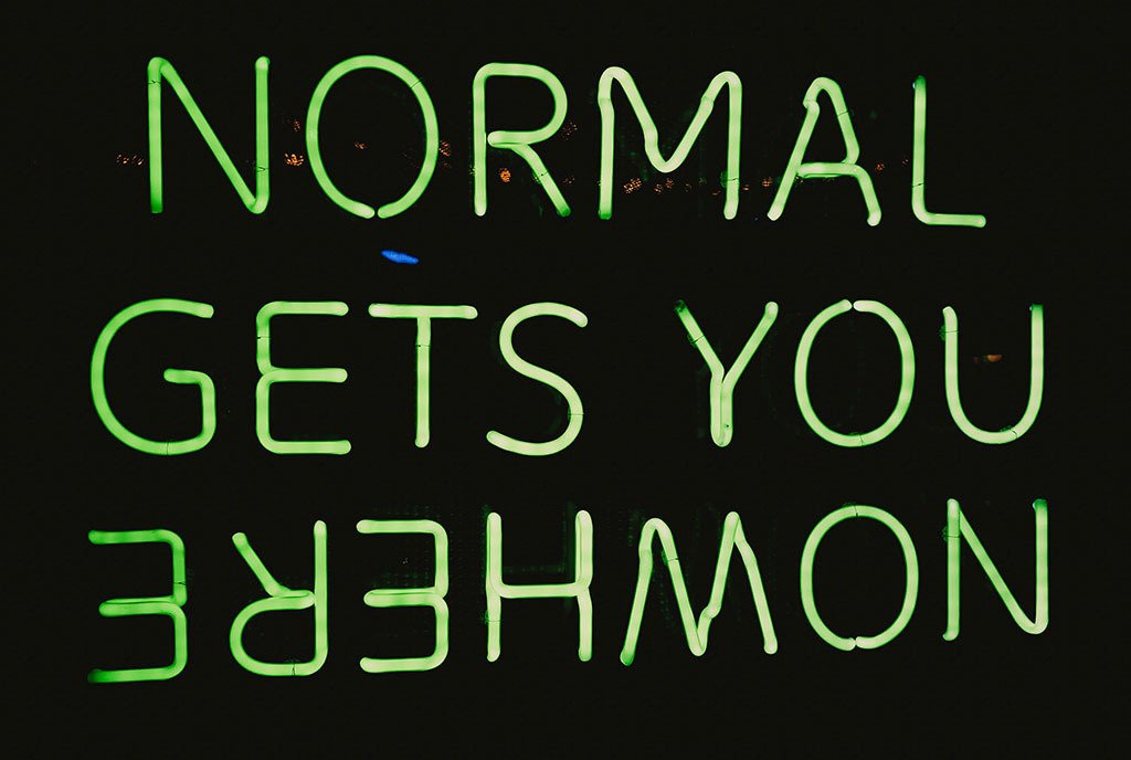 A green neon sign that reads, “Normal gets you Nowhere”. The word “Nowhere” is upside down.