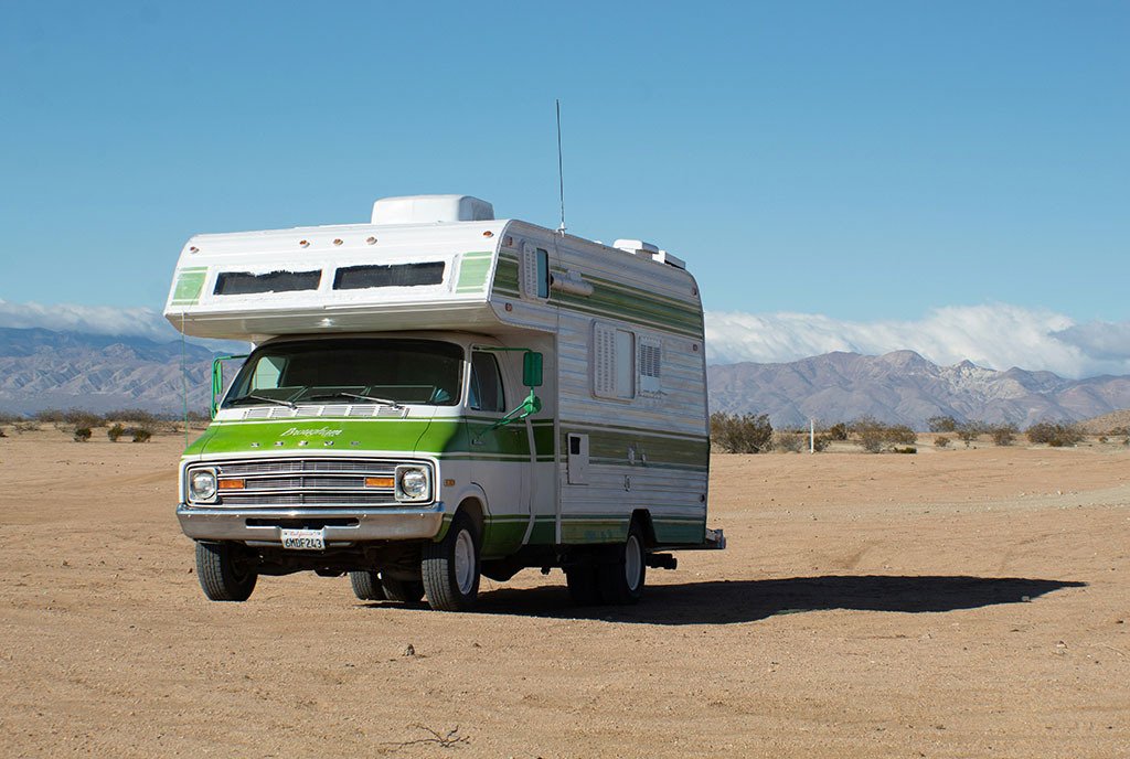 A white and green RV parked in the expanse of a Southwest American desert.