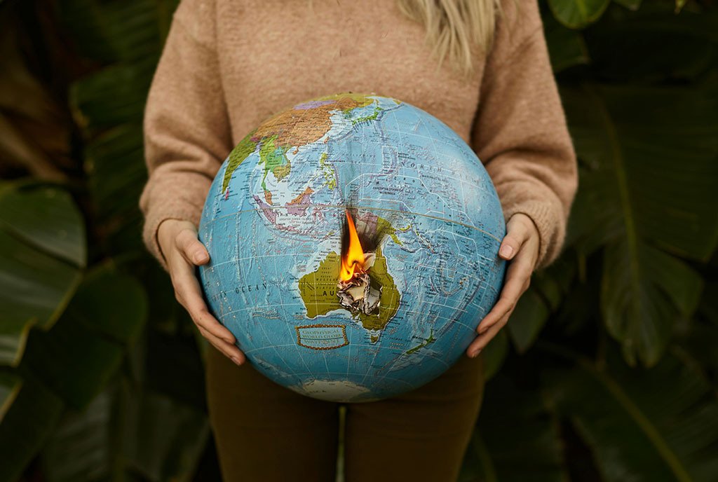 A woman’s hands hold a globe that is on fire. She stands in front of palm leaves.