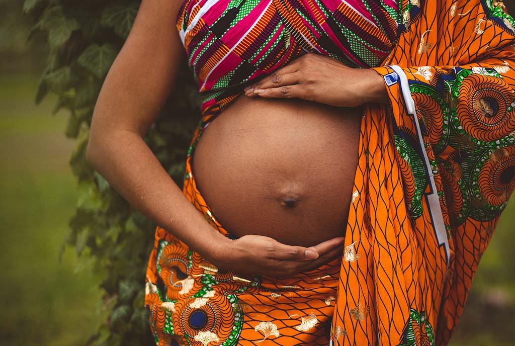 Close up shot of a Black pregnant woman holding her belly, wrapped in colorful ankara prints.