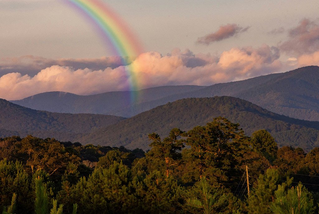 An image of the Appalachian mountains on at dusk, with a rainbow tucked behind a mountain, reaching to the sky.