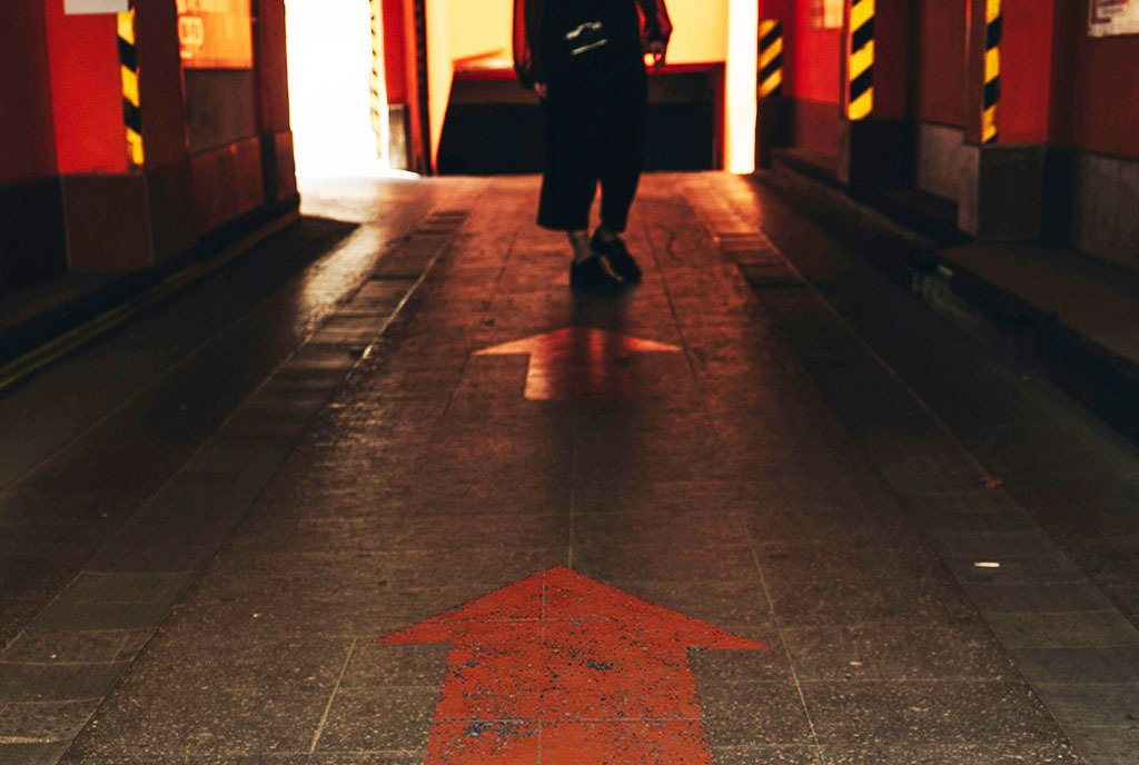 A close-up shot of a person walking along a path with arrows pointing forward, guiding their way.